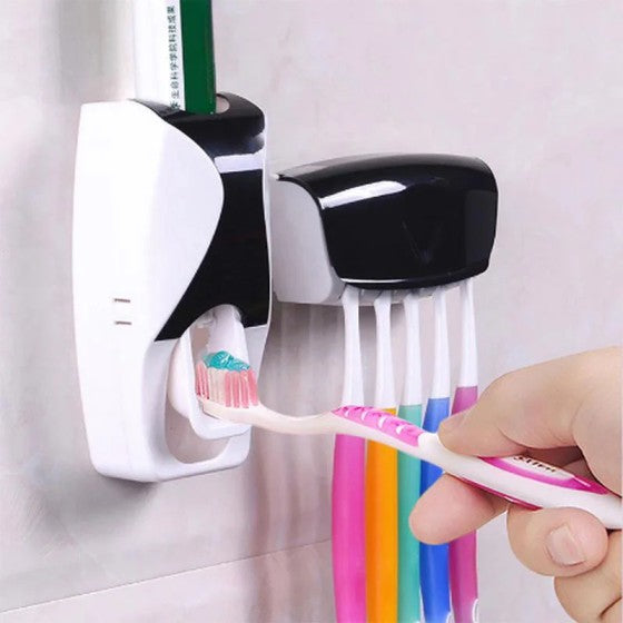 Wall-mounted toothpaste dispenser and holder with multiple toothbrushes and a hand holding a colorful toothbrush.