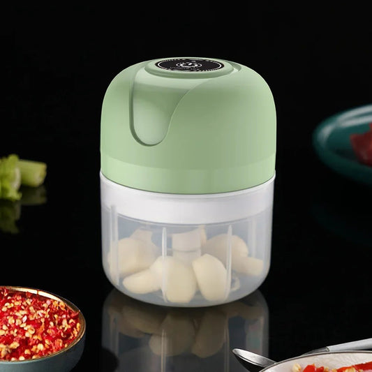 Green mini electric chopper with chopped garlic inside, surrounded by ingredients on a dark background